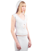 Woman wearing a white sleeveless top with a unique cutout design on a white background